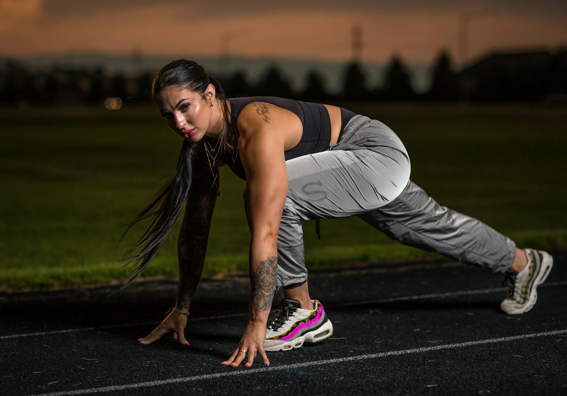 Biegaczka w pozycji startowej na tartanowej bieżni o zmierzchu