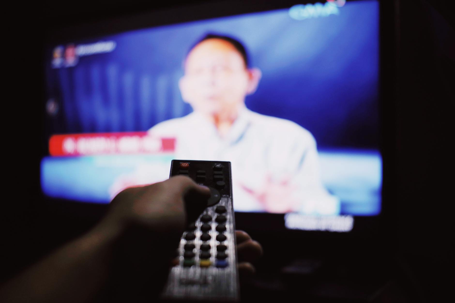 Osoba z pilotem zmienia kanały, oglądając telewizję w ciemnym salonie