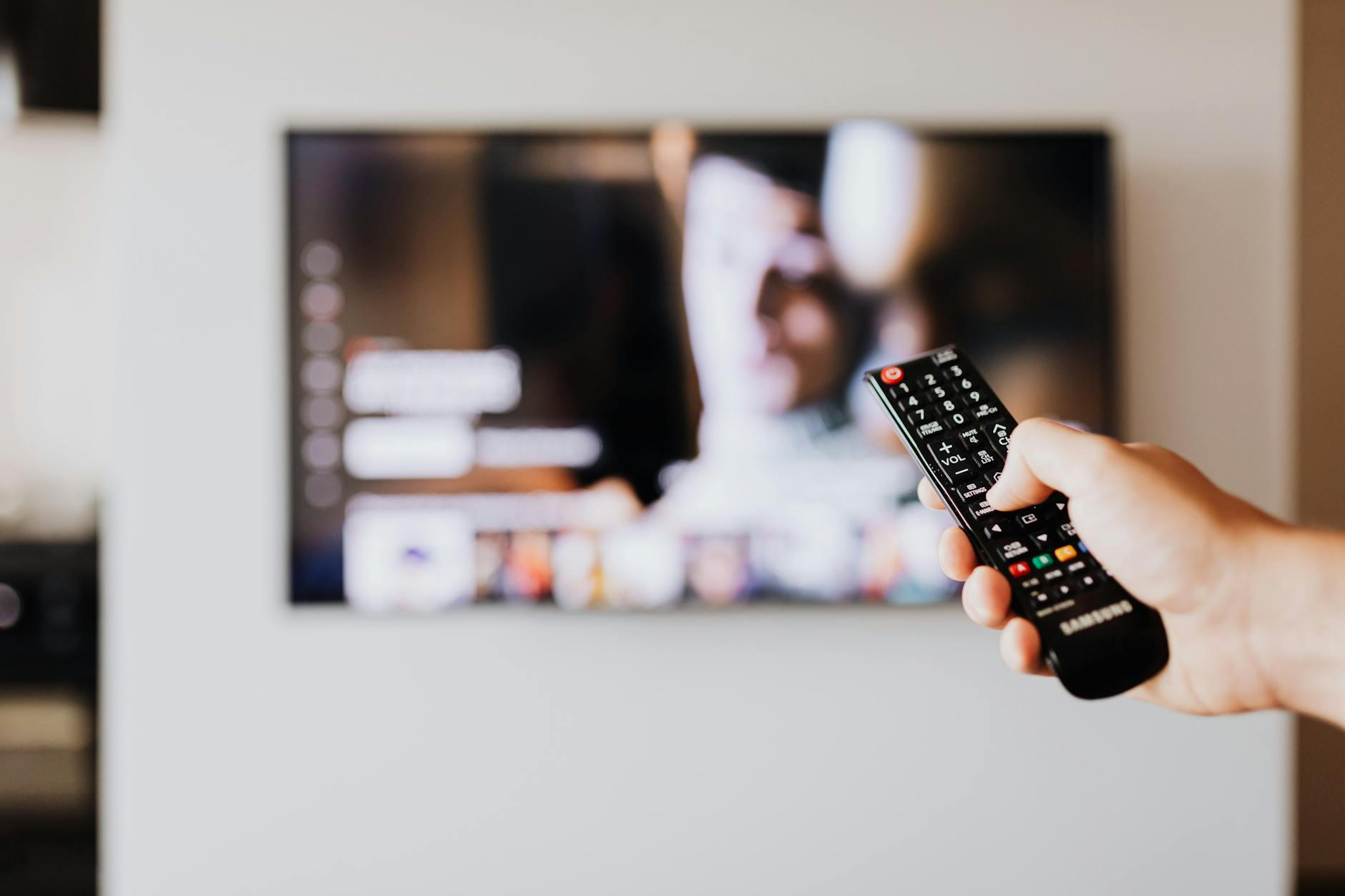 Ręka z pilotem skierowanym w stronę włączonego telewizora